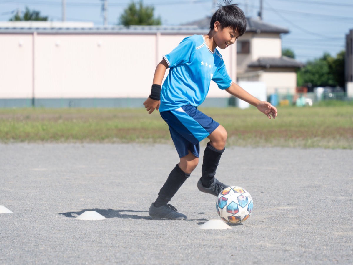 コーンの間でドリブルをする少年サッカー選手
